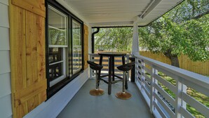 A covered porch with a wooden table and two chairs, a white railing, and a view of trees. - The Spruce House Cozy Home in Swannanoa (Swannanoa)