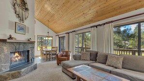 Ein gemütliches Wohnzimmer mit Kamin aus Stein, Holzbalkendecke, großem Fenster mit Vorhängen und einer bequemen Couch.
