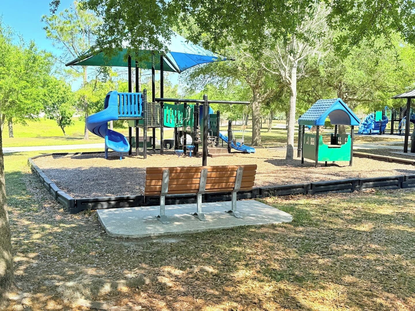 A playground with slides and climbing structures, surrounded by trees and a bench.