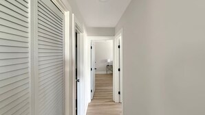 Un pasillo con paredes blancas, piso de madera y puertas cerradas con manijas negras.