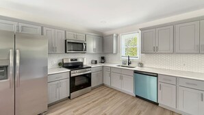 Una cocina moderna con electrodomésticos de acero inoxidable, armarios blancos y piso de madera.