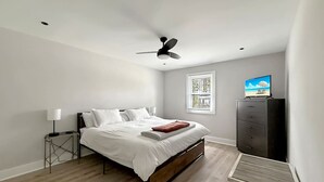 Un dormitorio con una cama, ventilador de techo, televisor y una mesita.