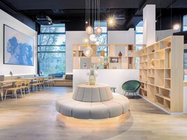 Ein modernes Interieur mit einer zentralen Sitzecke, Holzbücherregalen und großen Fenstern.