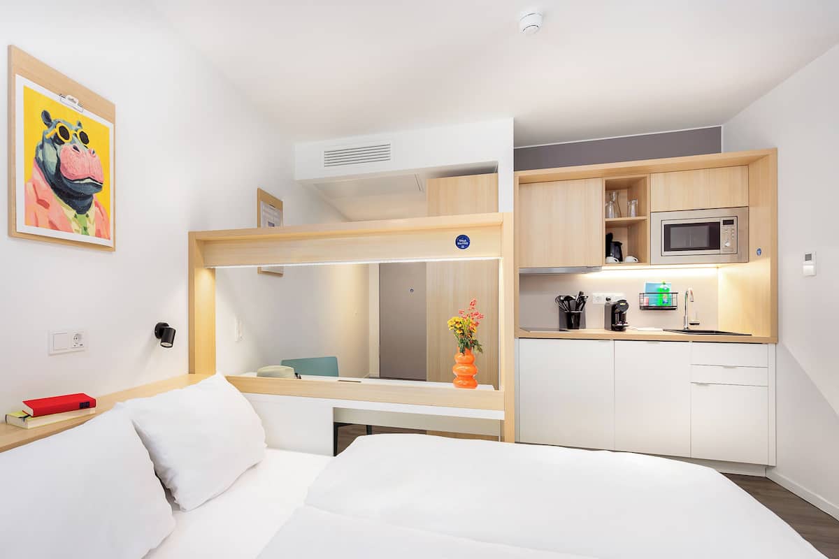 Ein modernes Hotelzimmer mit Bett, einer kleinen Küchenzeile und einem Badezimmer.
