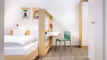 A modern bedroom with a bed, a desk, and a chair. There are two paintings on the wall.