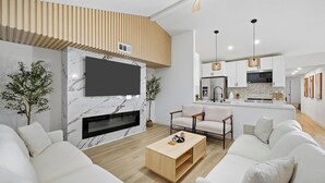 Een moderne woonkamer met een flatscreen televisie, een open haard en een keuken op de achtergrond.