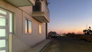 A building with a garage door, a balcony, and a parked car. - Charming 2-bedroom apartment with Valley Views in Kerċem (Kercem)