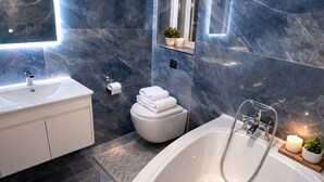 A modern bathroom with a large bathtub, a white toilet, a vanity with a mirror, and marble walls. - Charming 2-bedroom apartment with Valley Views in Kerċem (Kercem)