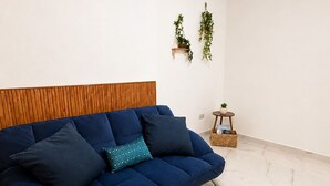 A modern living room with a blue sofa, a wooden headboard, a hanging light fixture, and a small side table with a plant. - Charming 2-bedroom apartment with Valley Views in Kerċem (Kercem)