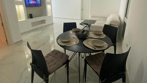 A modern dining area with a round table, chairs, and a flat-screen TV mounted on the wall. - Charming 2-bedroom apartment with Valley Views in Kerċem (Kercem)