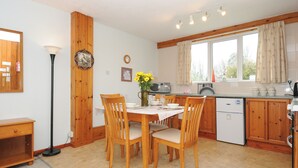 Een keuken met houten kastjes, een eettafel met stoelen, een klok en een raam met gordijnen.