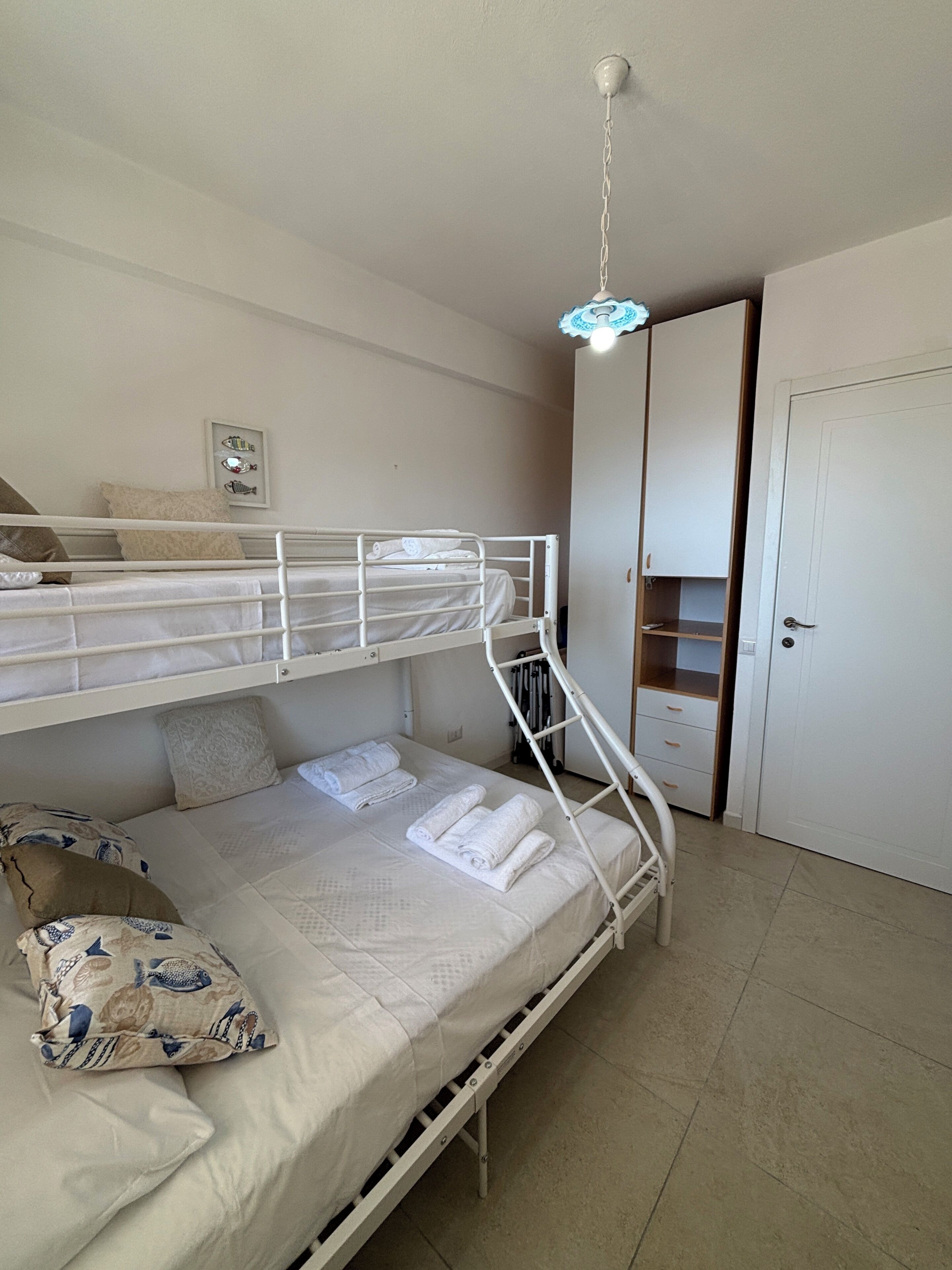 Une chambre avec un lit superposé, un ventilateur de plafond, une porte et un petit placard.