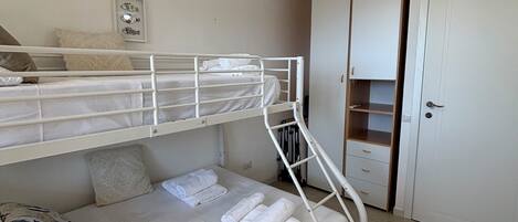 Une chambre avec un lit superposé, un ventilateur de plafond, une porte et un petit placard.