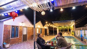 Um pátio externo com piscina, paredes de tijolo e luzes de corda.
