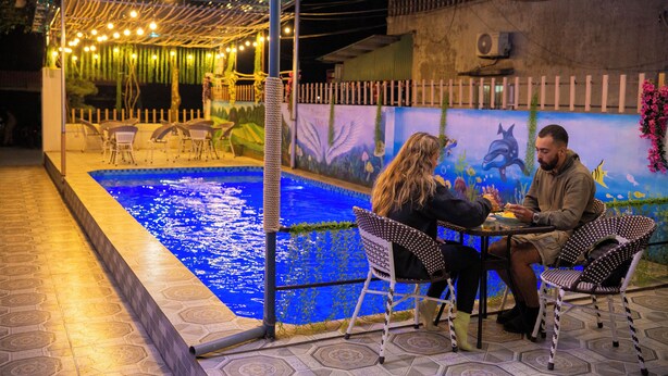 Área de refeições ao ar livre com piscina e um mural de criaturas marinhas.