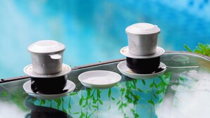 Duas chávenas de café preto e branco sobre uma mesa de vidro perto de uma piscina.