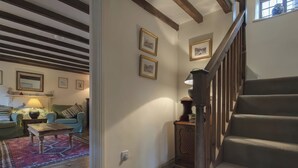 A cozy living room with a staircase, wooden beams, and framed pictures on the walls.