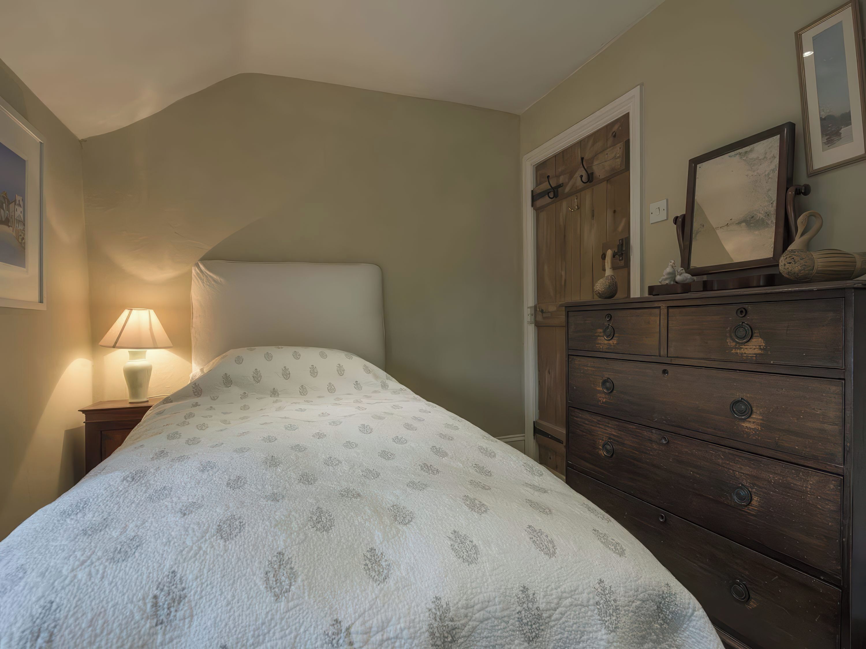 Une chambre à coucher avec un lit, une commode, une lampe et un tableau encadré accroché au mur.