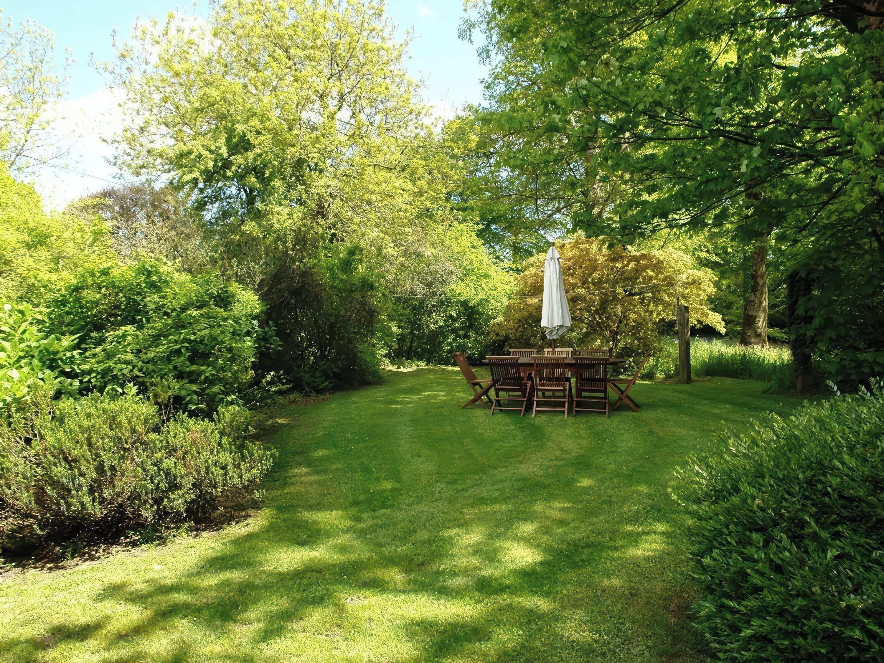 Ein Garten mit einem Holztisch und Stühlen, umgeben von üppigem Grün und Bäumen.