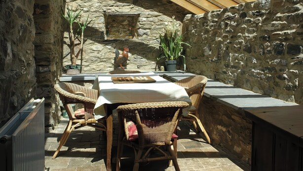 A stone-walled patio with wicker furniture, a table, and potted plants.