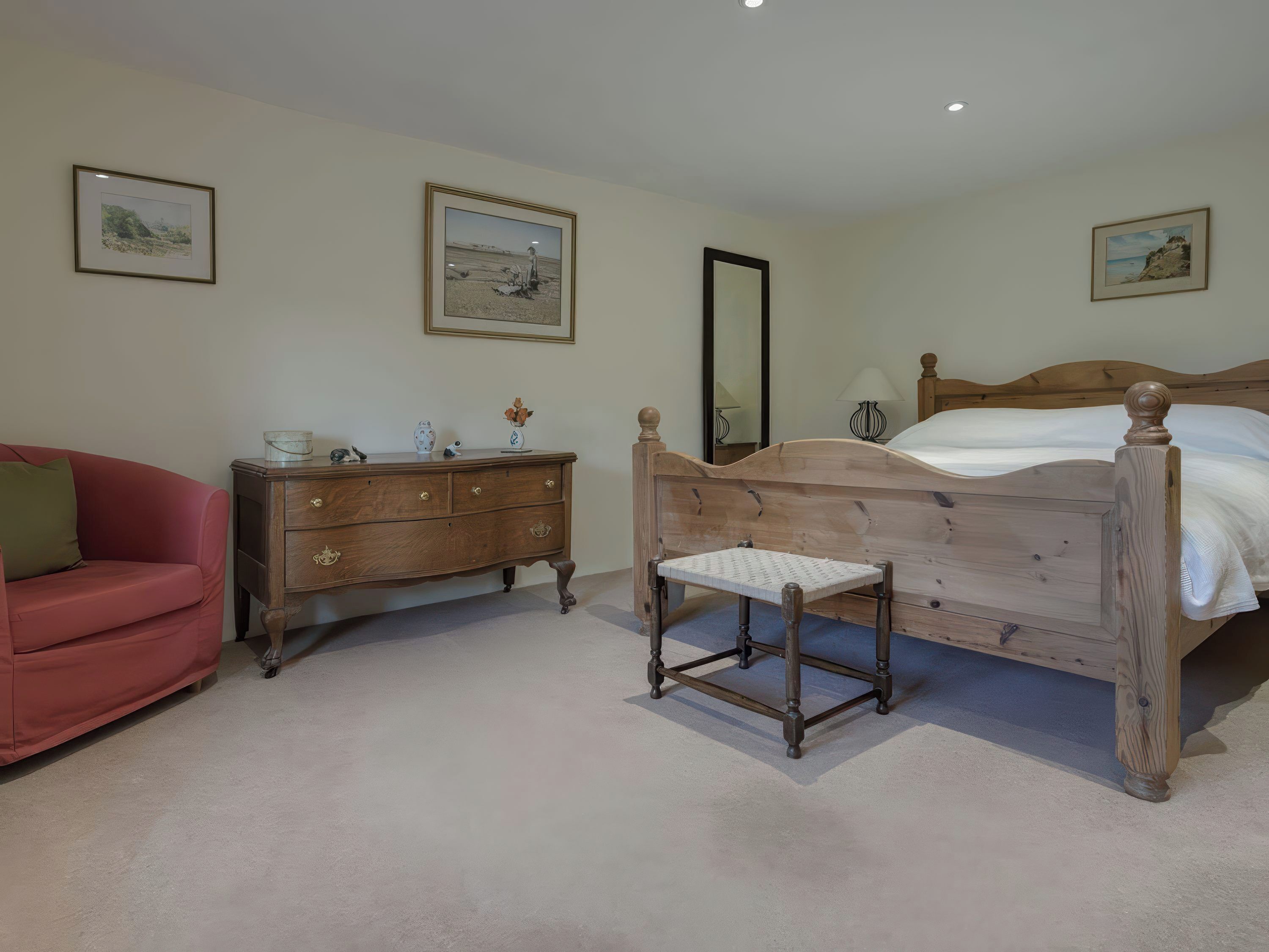 A bedroom with a wooden bed, a wooden dresser, a red sofa, and three framed pictures on the walls.