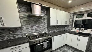 A modern kitchen with white cabinets, a stainless steel stove, and a marble backsplash. - Smethwick - House - Sleeps 8 - Parking (Smethwick)