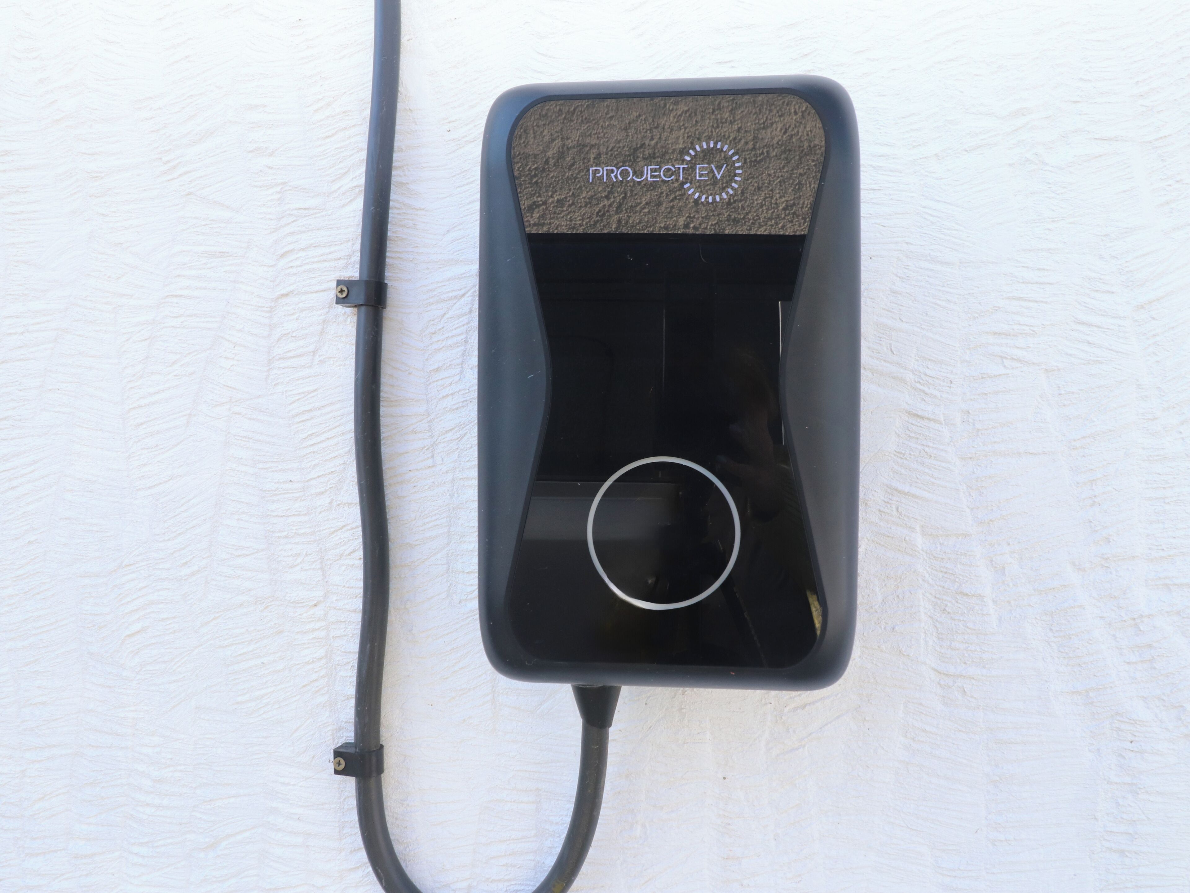 Une prise électrique noire avec un câble branché, portant l’inscription « PROJET VE ».