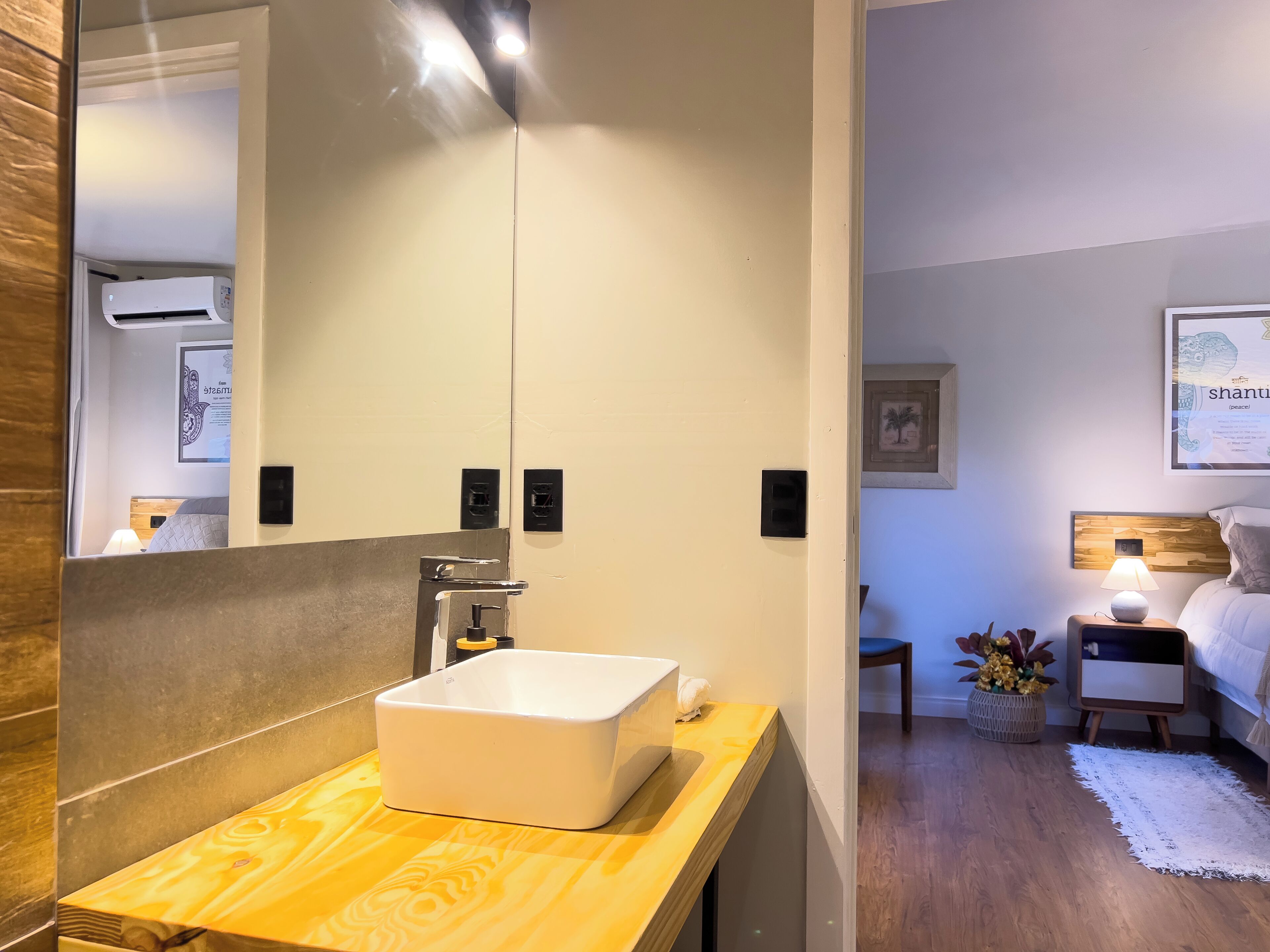 A modern bathroom with a large mirror, a white sink, and a wooden vanity.