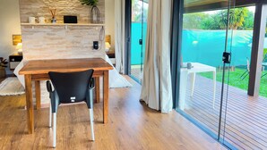 A modern kitchen with a stone backsplash, wooden dining table, and a view of a green garden through large sliding glass doors. - Charming Cottage on the São Roque Wine Route - Design and Nature in the Mountains (São Roque)
