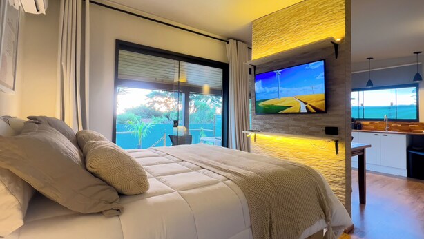 A modern bedroom with a large bed, a TV mounted on the wall, and a view of the outdoors. - Charming Cottage on the São Roque Wine Route - Design and Nature in the Mountains (São Roque)