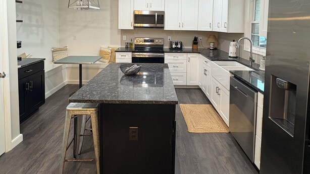 Una cocina moderna con armarios blancos, una isla central, electrodomésticos de acero inoxidable y piso de madera oscura.