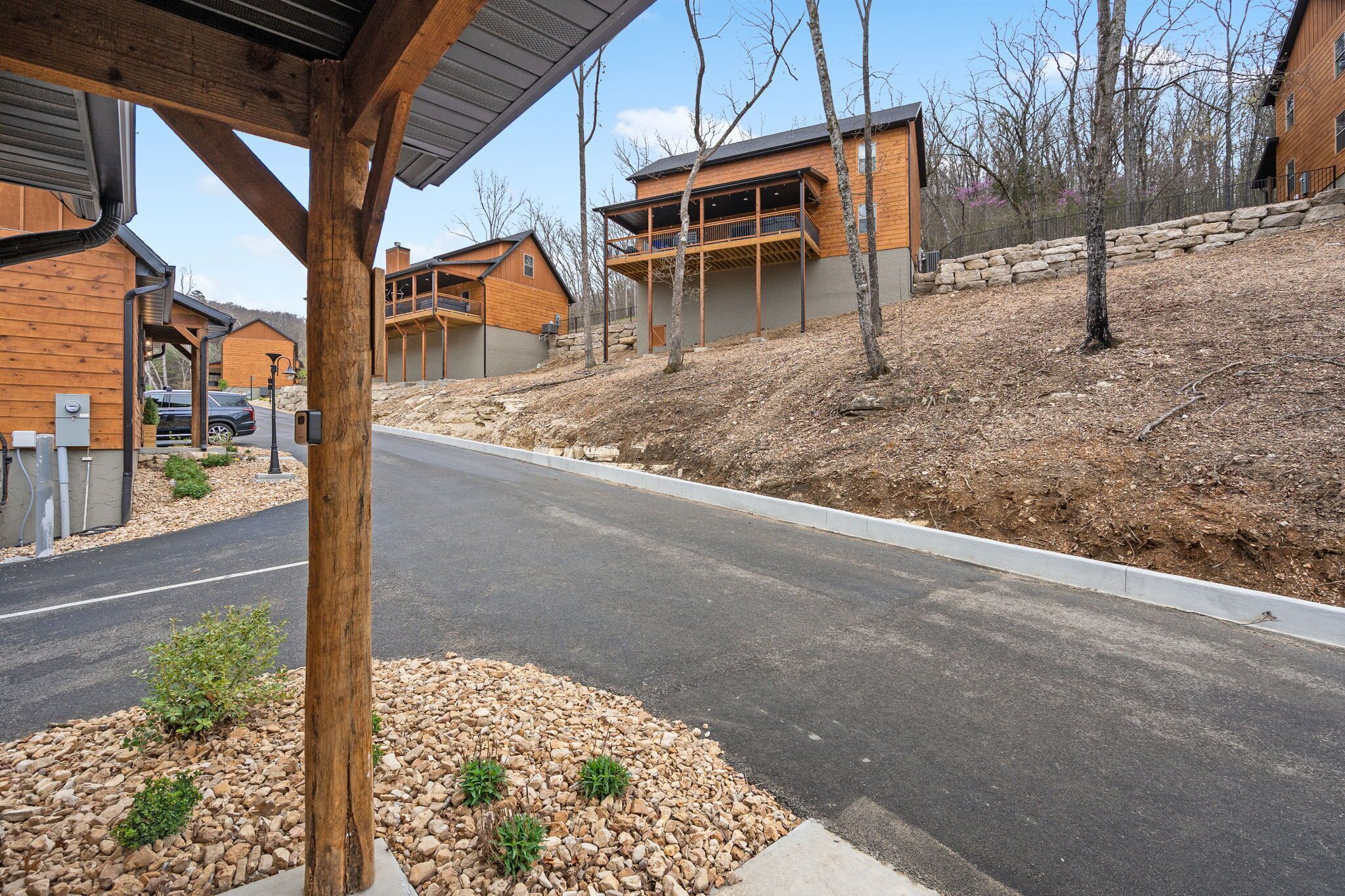 Un quartier résidentiel avec des maisons modernes en bois, une route asphaltée et un mur de soutènement en pierre.