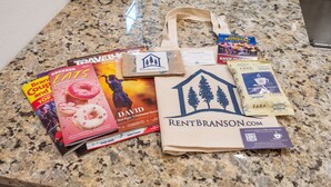 A granite countertop with various items including a RentBranson.com tote bag, a David book, a travel magazine, and coffee packets.