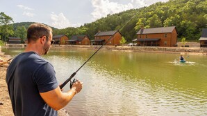 A man fishing by a calm lake with houses in the background.