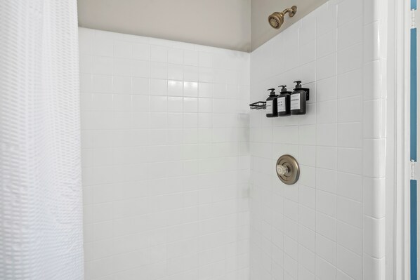 A bathroom with white tiled walls, a shower curtain, and two black soap dispensers mounted on the wall.