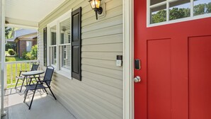 Una casa con puerta roja, un porche con mesa y sillas, y una ventana con lámpara.