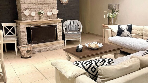 A living room with a stone fireplace, a white sofa, a patterned armchair, and a coffee table. - Charming 3-bedroom Penthouse with AC, WiFi in lovely Oroklini (Oroklini)