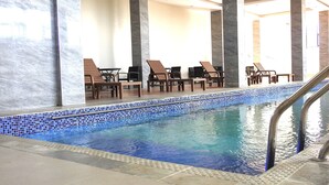 An indoor swimming pool with tiled blue edges, surrounded by lounge chairs and a tiled floor.