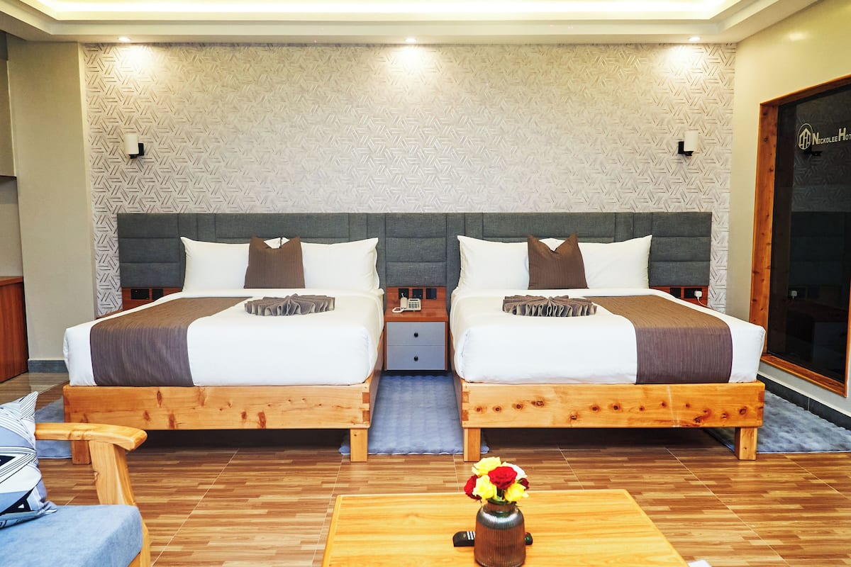 A hotel room with two beds, wooden headboards, a small bedside table with a phone, and a vase with flowers on a wooden table.