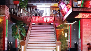 A staircase with a neon sign reading "CLUB YOYO" leading to a bar area with wooden tables and chairs.
