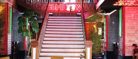 A staircase with a neon sign reading "CLUB YOYO" leading to a bar area with wooden tables and chairs.