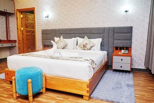 Una cama bien tendida con un cabecero gris, una mesita de noche de madera con una lámpara y un otoman azul.