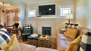 A living room with a fireplace, a television mounted above it, and a sofa with patterned cushions. - Les Petit Maison (Black Mountain)