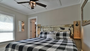 A bedroom with a checkered bedspread, a ceiling fan, a wooden headboard, and a mirror on the wall. - Les Petit Maison (Black Mountain)