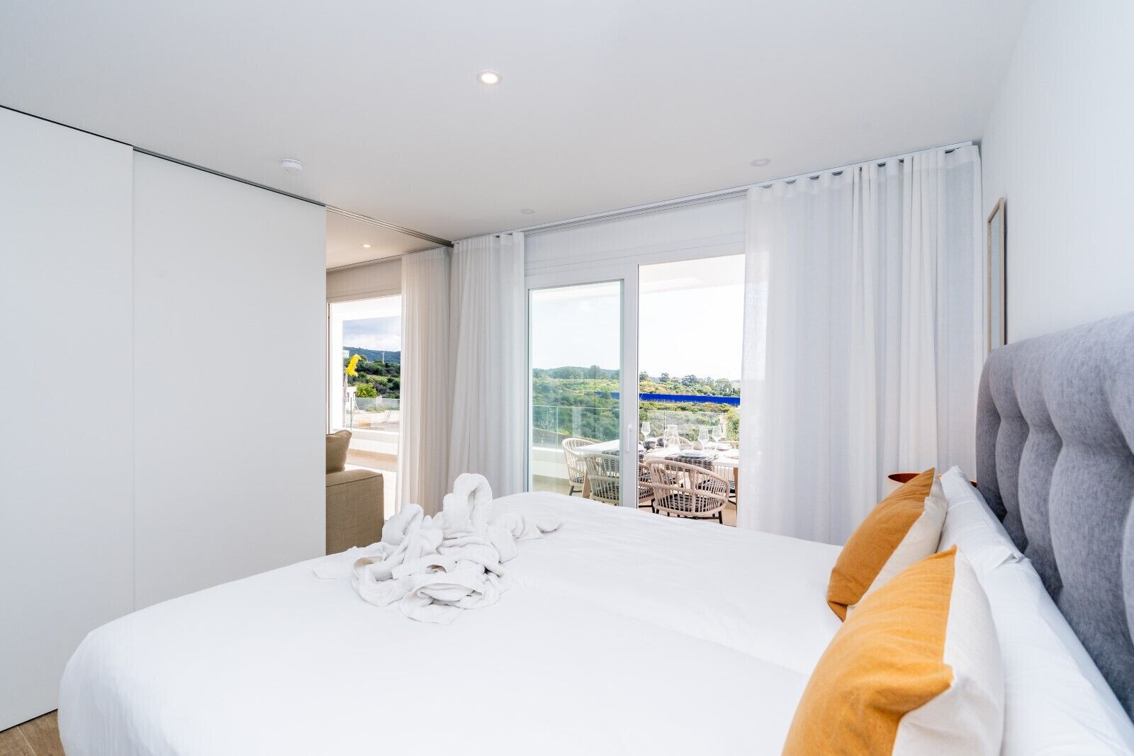 Ein modernes Hotelzimmer mit einem großen Bett, weißen Leinentextilien, einem grauen Kopfteil und einem Balkon mit Sitzgelegenheit im Freien.