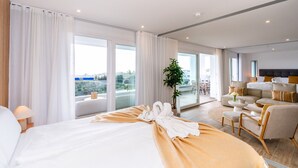 Ein modernes Hotelzimmer mit einem großen Bett, einer Sitzecke mit Sofa und Sesseln sowie einem Balkon mit Blick.