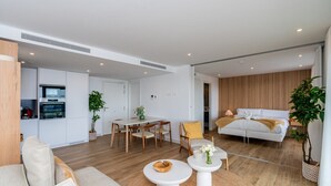 Ein modernes Wohnzimmer mit Sofa, Couchtisch, Esstisch und ein Schlafzimmer mit Bett und Nachttisch.