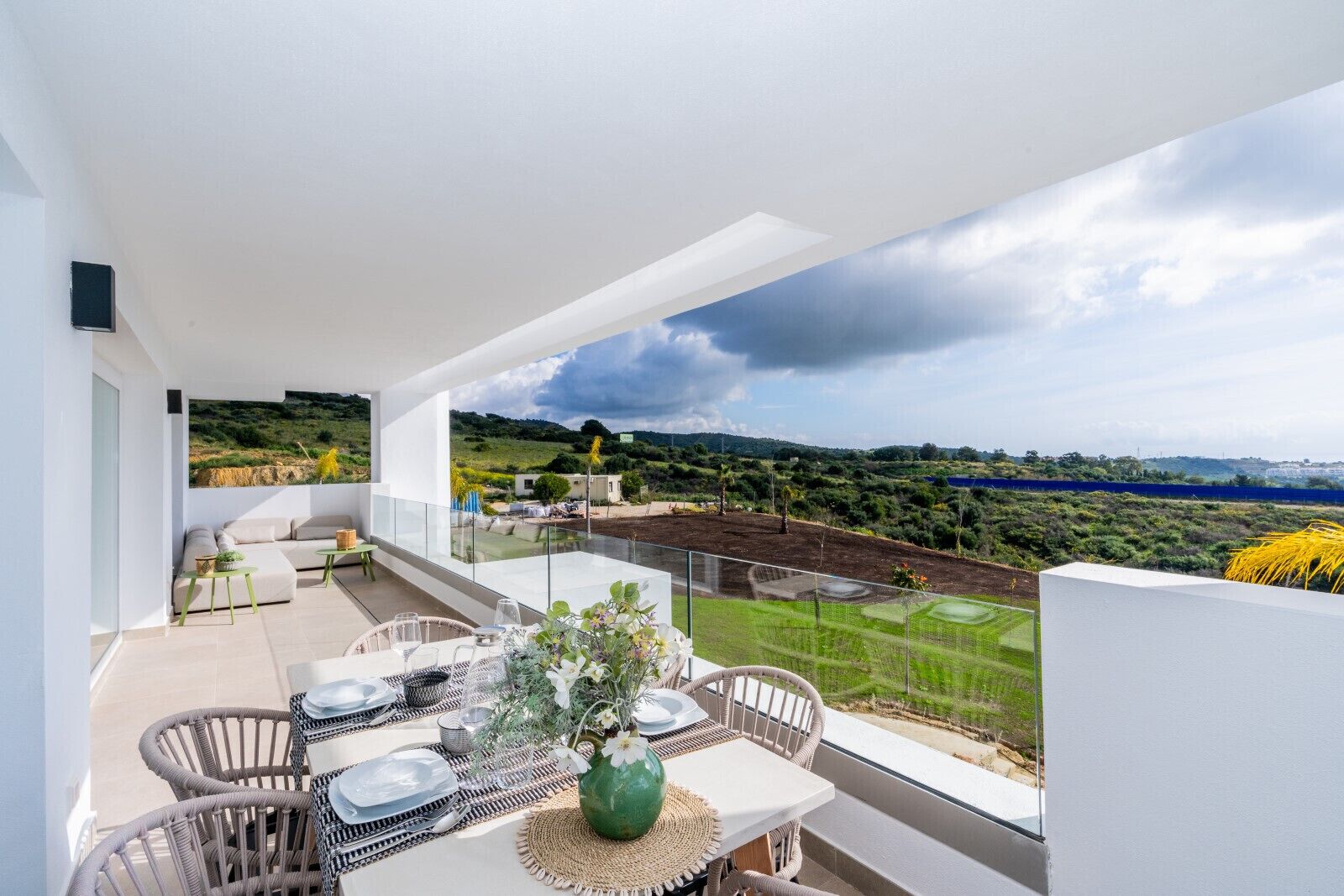 A balcony with a dining table set for four, overlooking a scenic landscape with hills and a body of water.