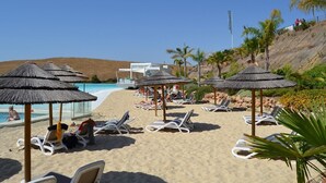 Ein Strandresort mit Liegestühlen, Reetdachsonnenliegen und einem Poolbereich.