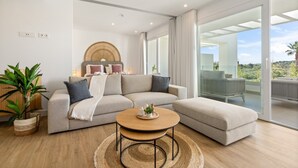 Ein modernes Wohnzimmer mit einem Ecksofa, einem runden Couchtisch und einer großen Schiebetür, die auf einen Balkon führt.